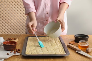Photo of Making delicious baklava. Woman buttering dough at wooden table, closeup