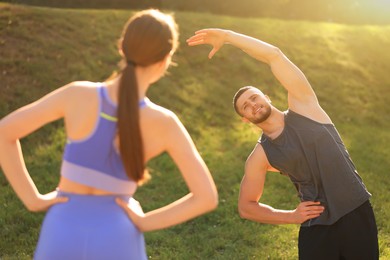 Photo of Attractive couple doing sports exercises in park on sunny day. Stretching outdoors