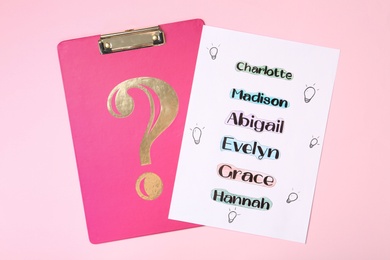 List of different baby names and clipboard on pink background, top view