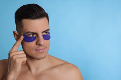 Photo of Man applying under eye patch on light blue background. Space for text