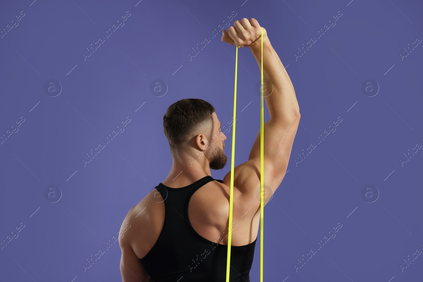 Photo of Muscular man exercising with elastic resistance band on purple background, back view