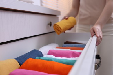 Woman putting rolled shirt into drawer at home, closeup. Organizing clothes