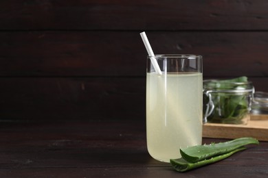 Photo of Tasty aloe juice in glass and cut fresh leaves on wooden table, space for text