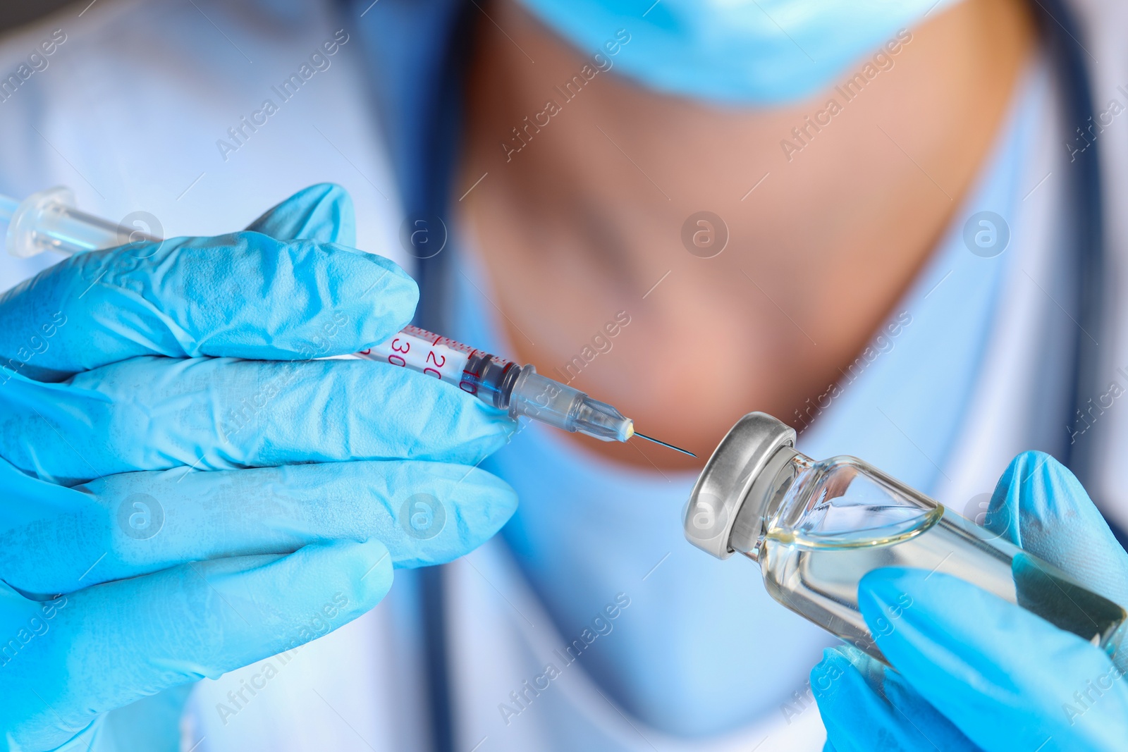 Photo of Doctor inserting syringe into glass vial with medication, closeup