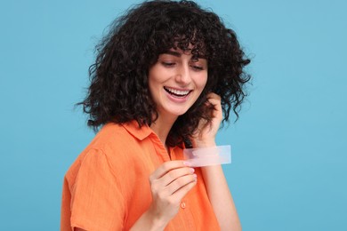 Photo of Young woman holding teeth whitening strips on light blue background