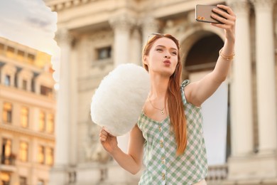 Photo of Woman with cotton candy taking selfie on city street. Space for text