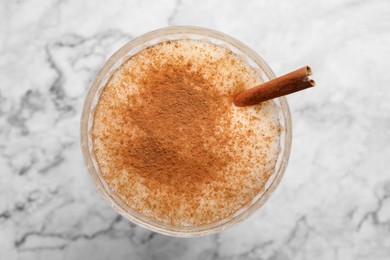 Photo of Delicious eggnog with cinnamon on white marble table, top view
