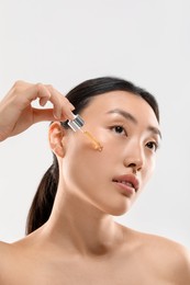 Beautiful young woman applying cosmetic serum onto her face on white background