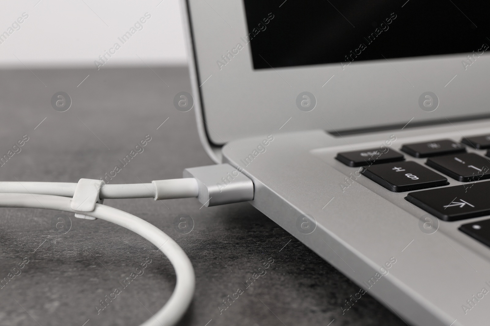 Photo of Modern laptop and charging cable on grey table, closeup