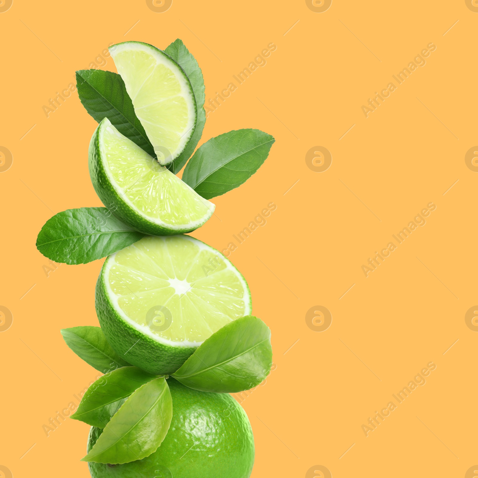 Image of Stacked cut and whole limes with green leaves on orange background, space for text