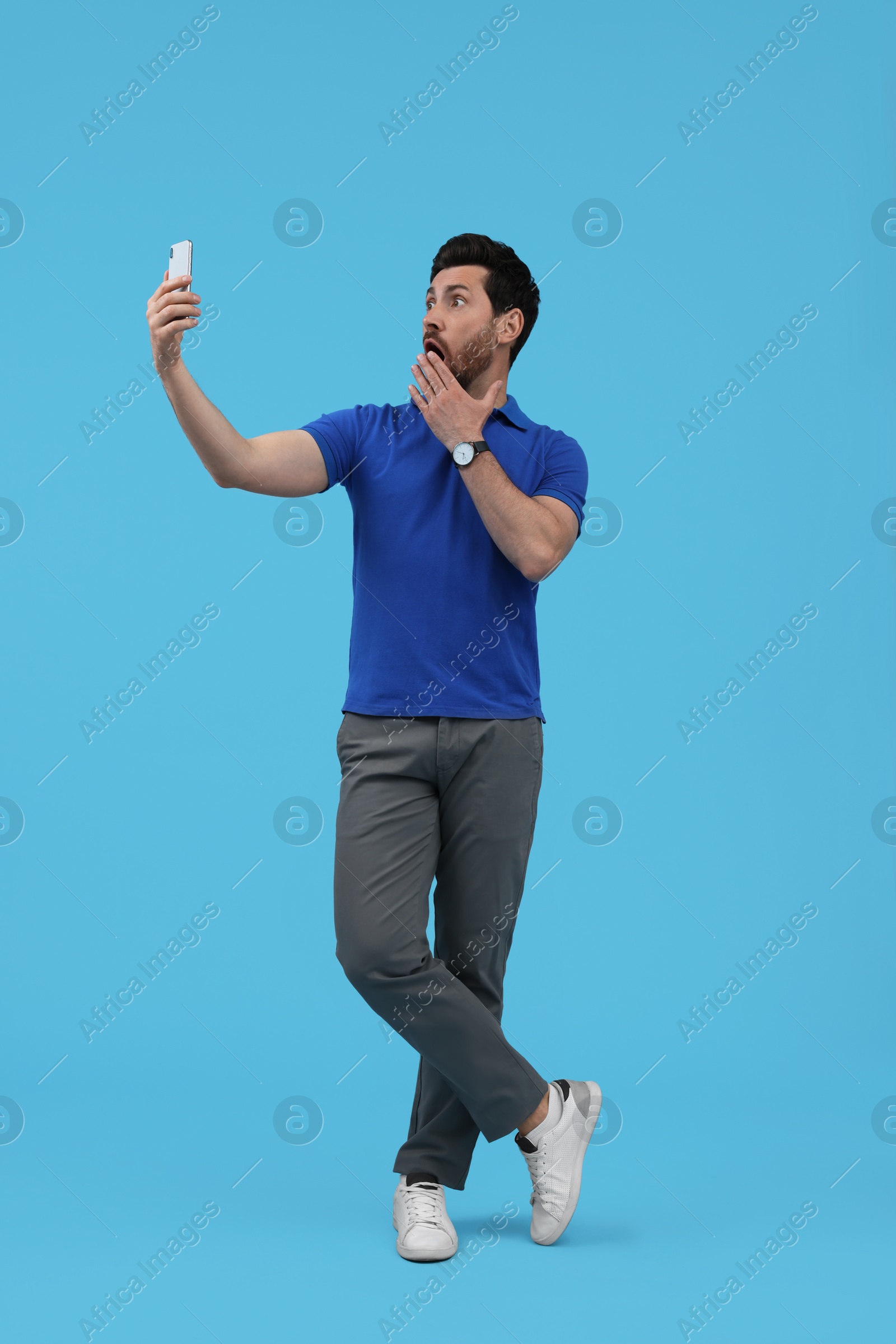 Photo of Surprised man taking selfie with smartphone on light blue background