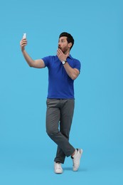 Photo of Surprised man taking selfie with smartphone on light blue background