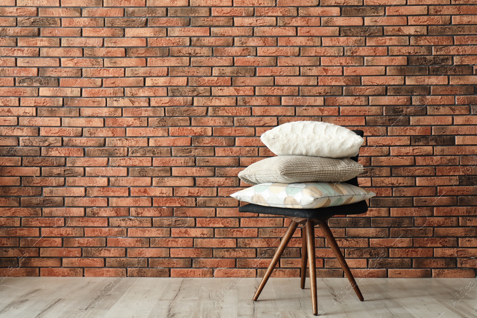 Photo of Stack of pillows on chair near brick wall