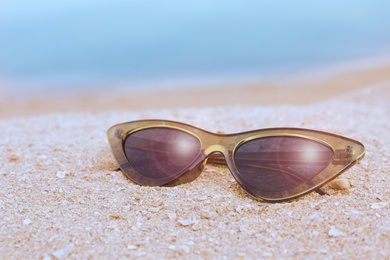 Stylish sunglasses on sandy beach near sea