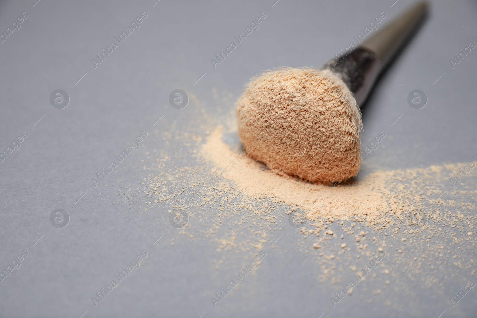 Photo of Loose face powder and makeup brush on light grey background, closeup. Space for text