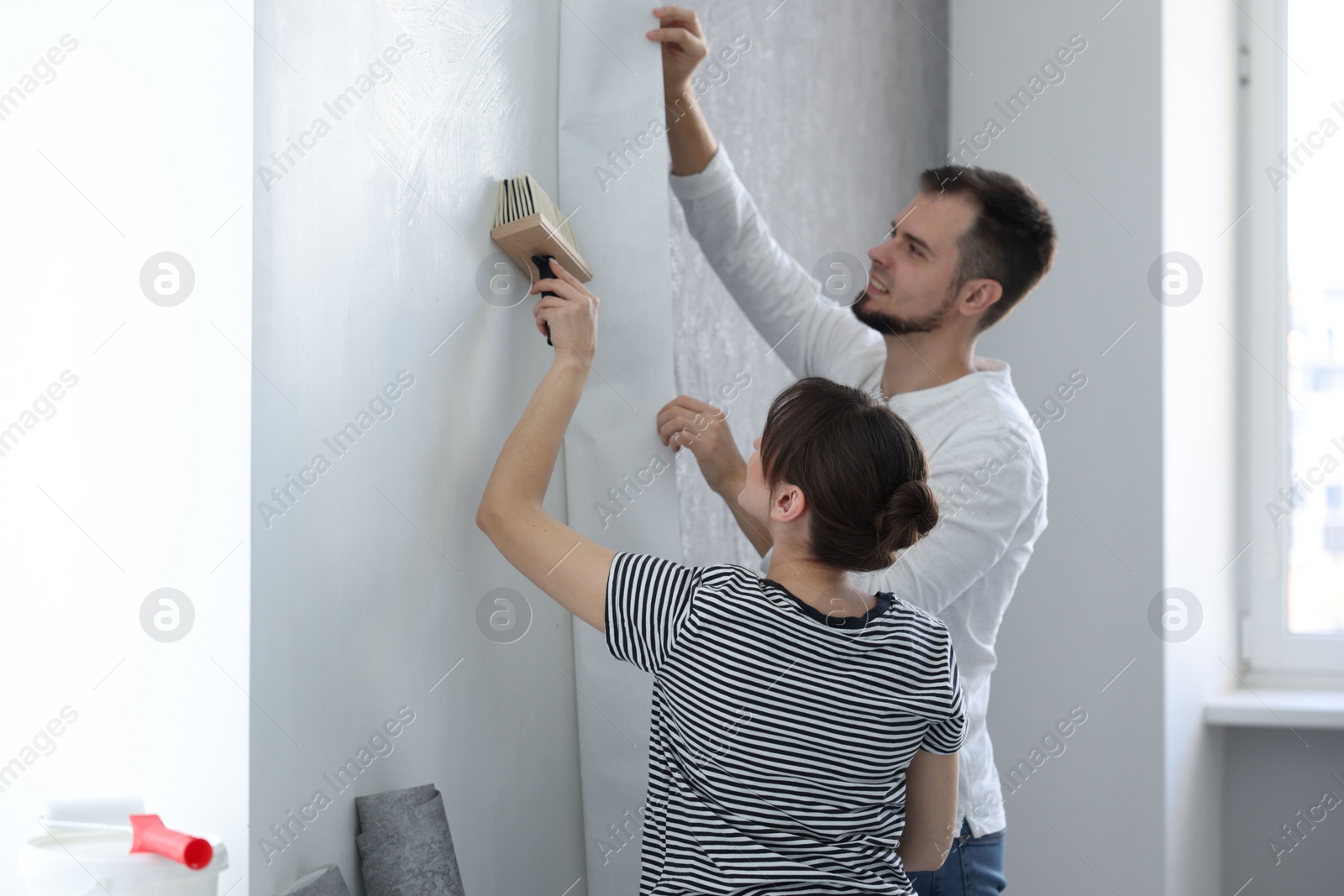 Photo of Woman and man hanging wallpaper in room