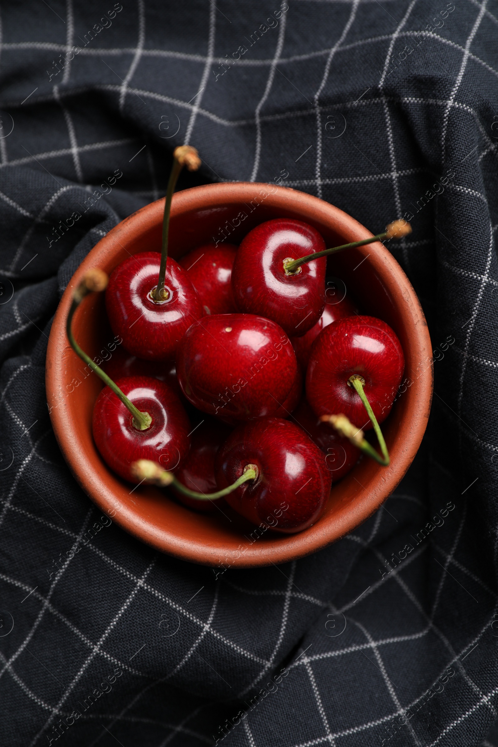 Photo of Sweet red cherries in bowl on black fabric, top view