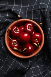 Photo of Sweet red cherries in bowl on black fabric, top view