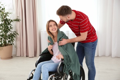 Photo of Man covering woman in wheelchair with plaid at home. Helping disabled