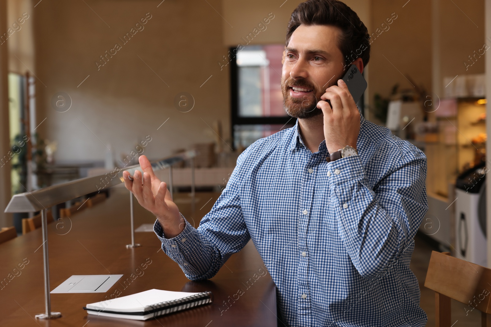 Photo of Handsome man talking on phone at table in cafe