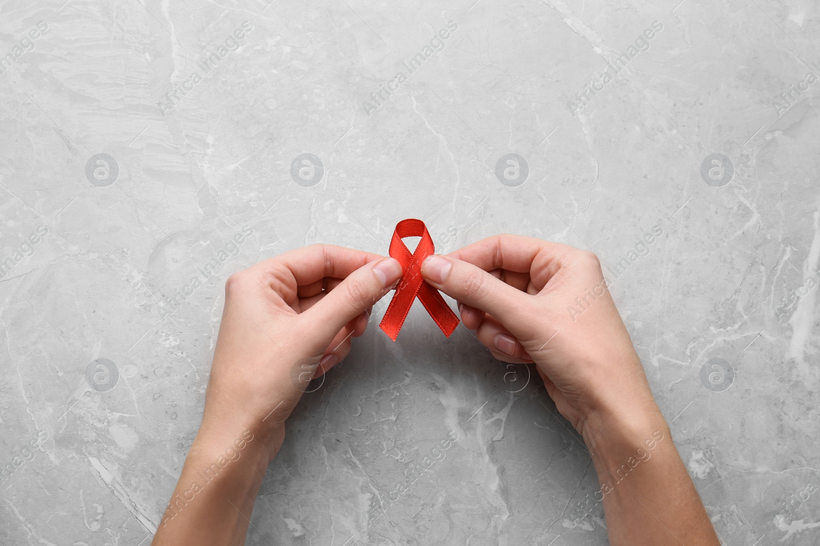 Photo of Woman holding red awareness ribbon at light grey marble table, top view. World AIDS disease day