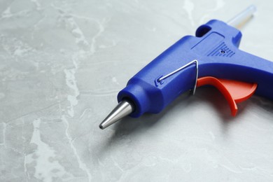 Photo of Blue glue gun with stick on light grey marble table, closeup. Space for text