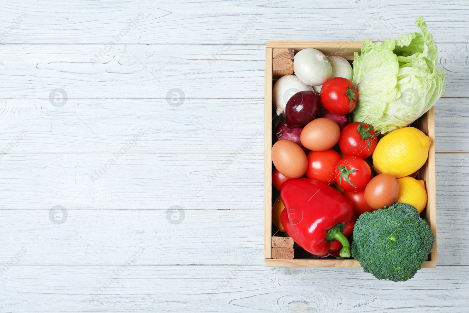 Photo of Wooden crate full of fresh products on light background, top view. Space for text