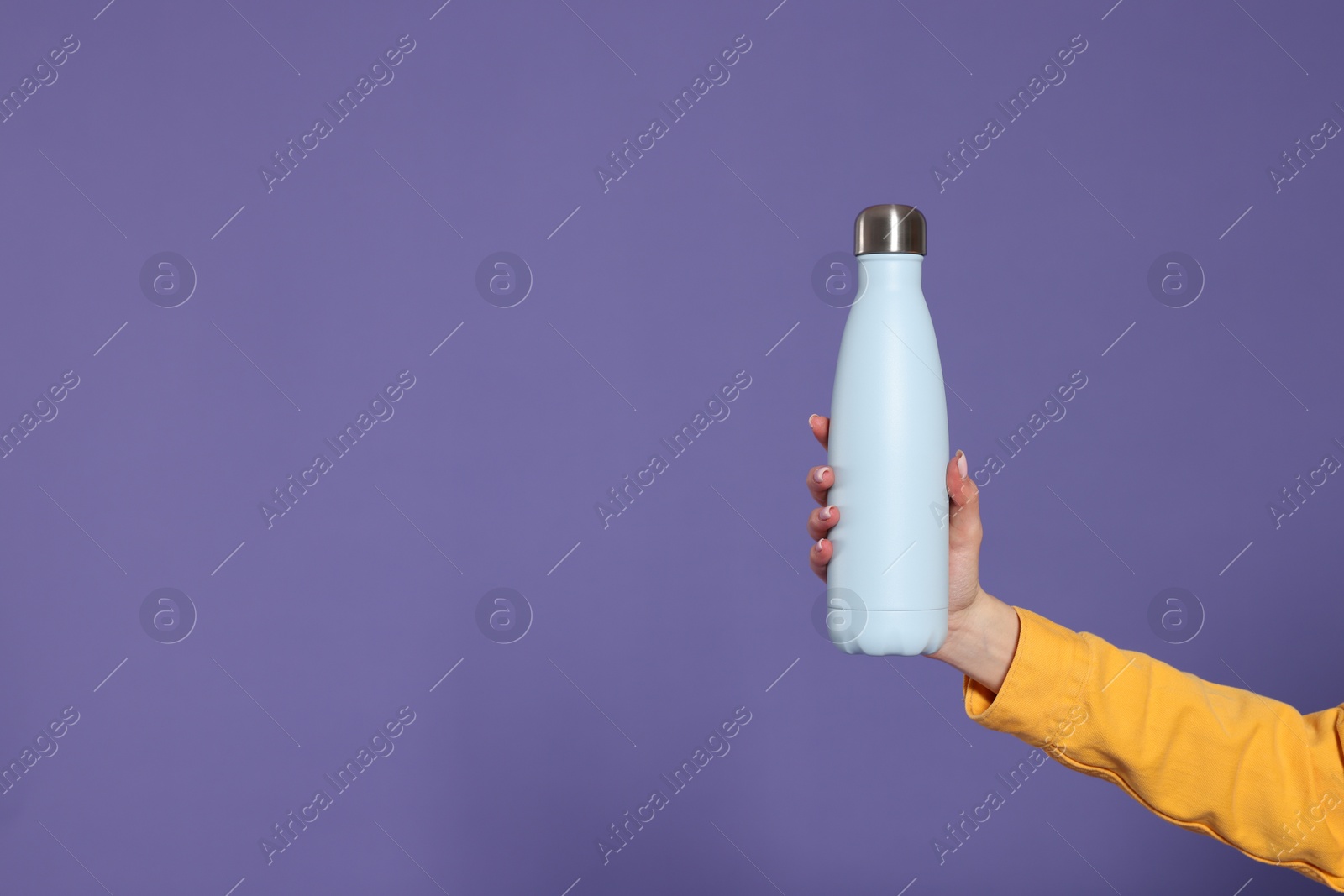 Photo of Woman holding thermos bottle on purple background, closeup. Space for text