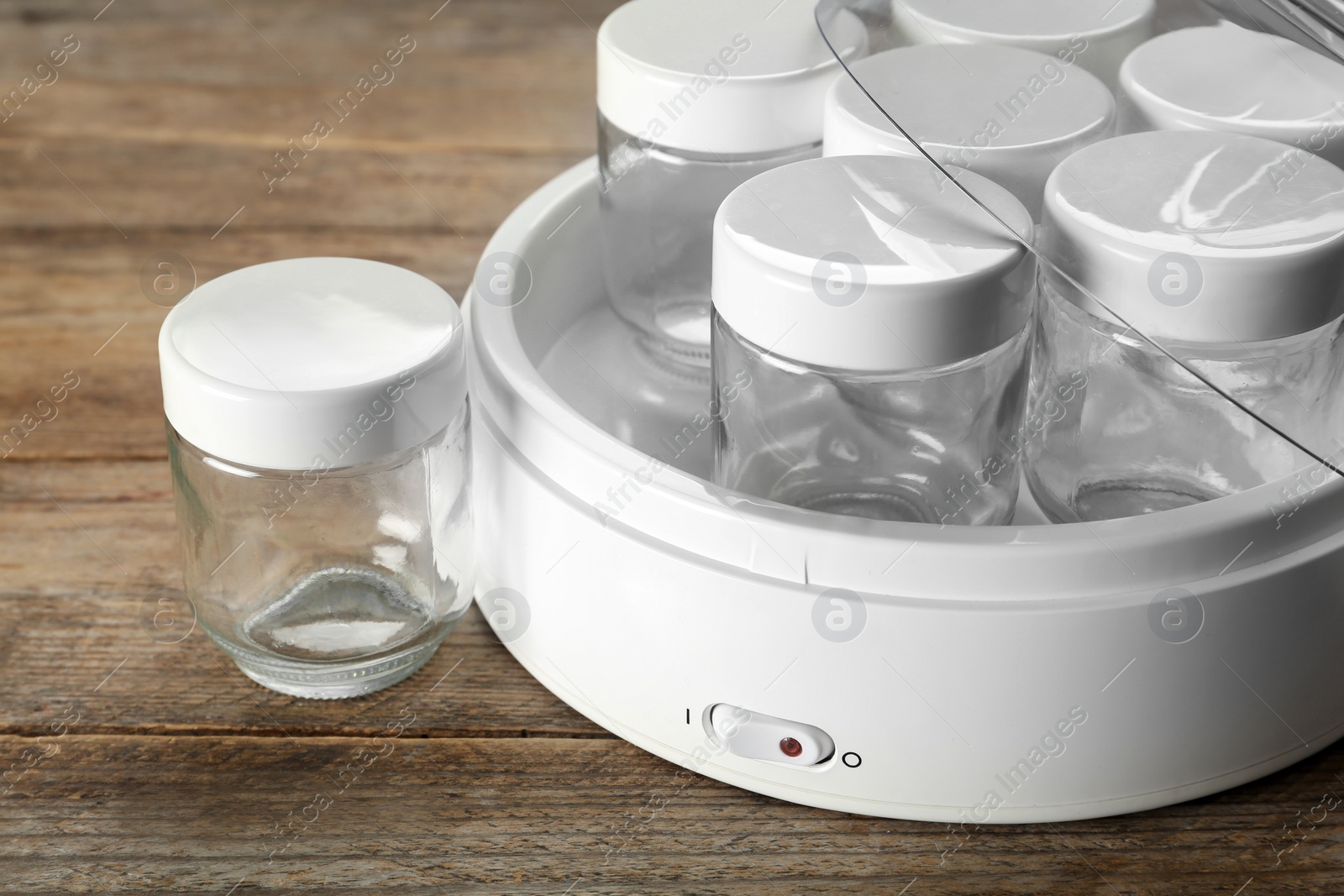 Photo of Modern yogurt maker with empty jars on wooden table, closeup