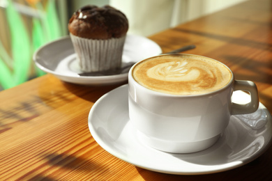 Cup of fresh aromatic coffee and cupcake at table in cafe