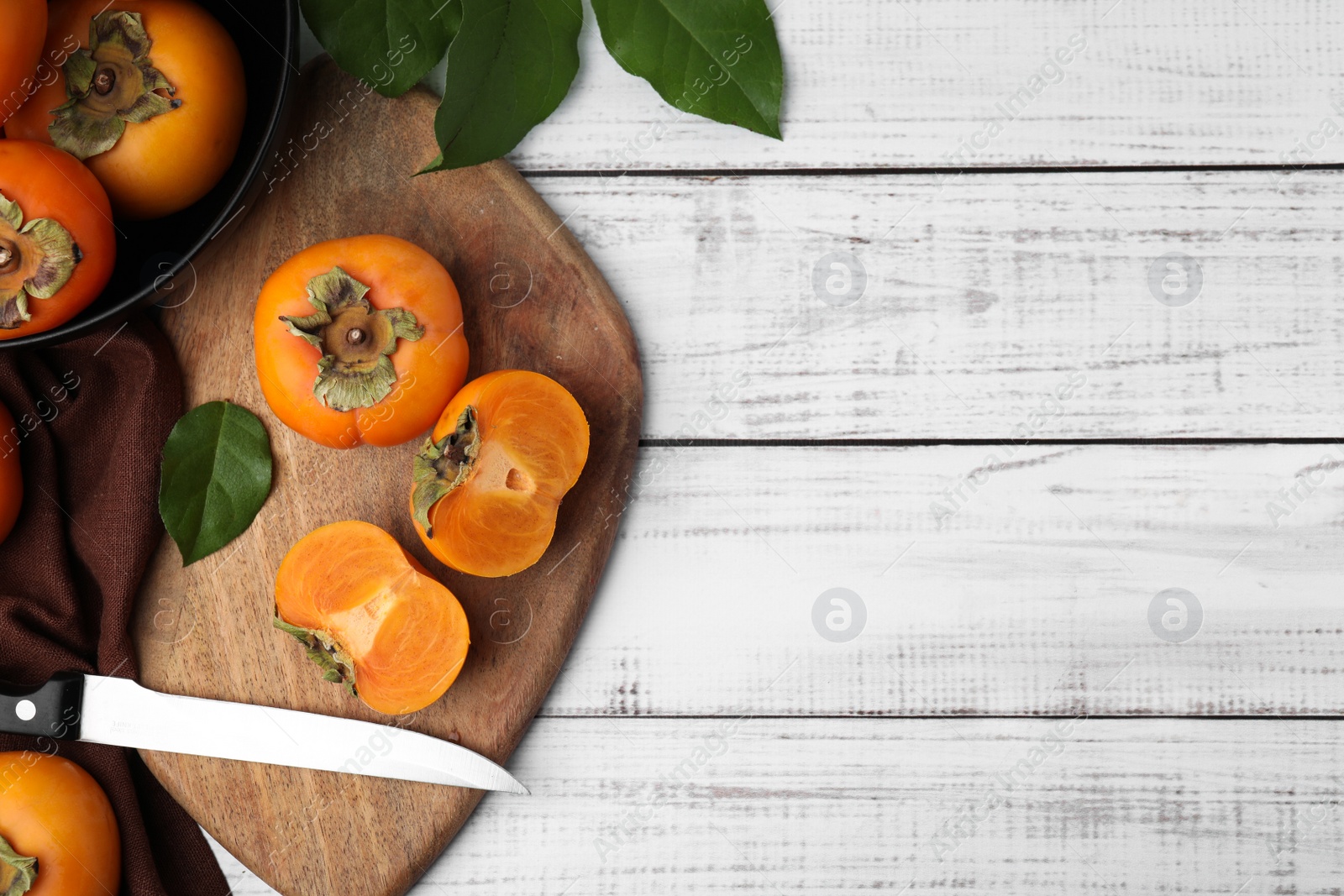 Photo of Whole and cut delicious ripe persimmons on white wooden table, flat lay. Space for text