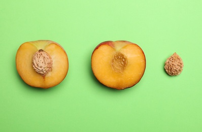 Photo of Halves of sweet juicy peach and stones on green background, top view