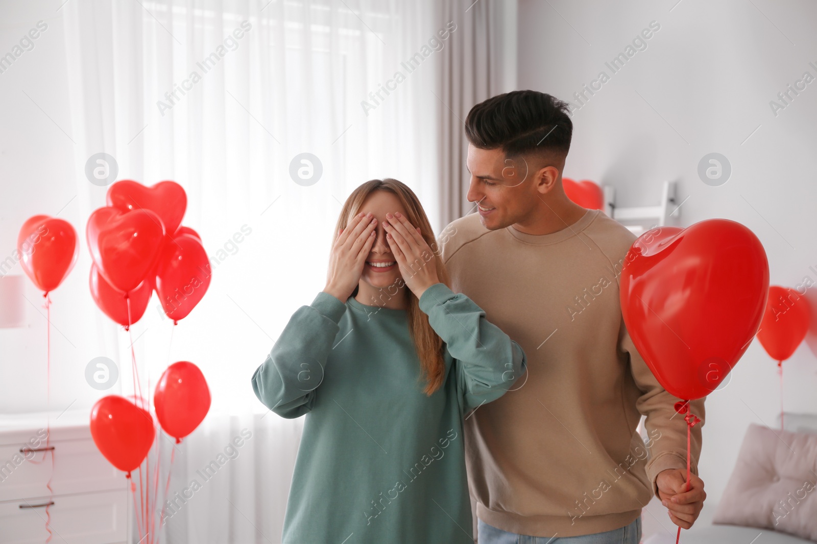 Photo of Man surprising his girlfriend with heart shaped balloon indoors. Valentine's day celebration