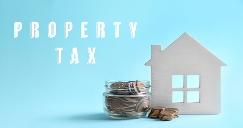 Image of Text Property Tax near jar full of coins and house model on light blue background. Banner design