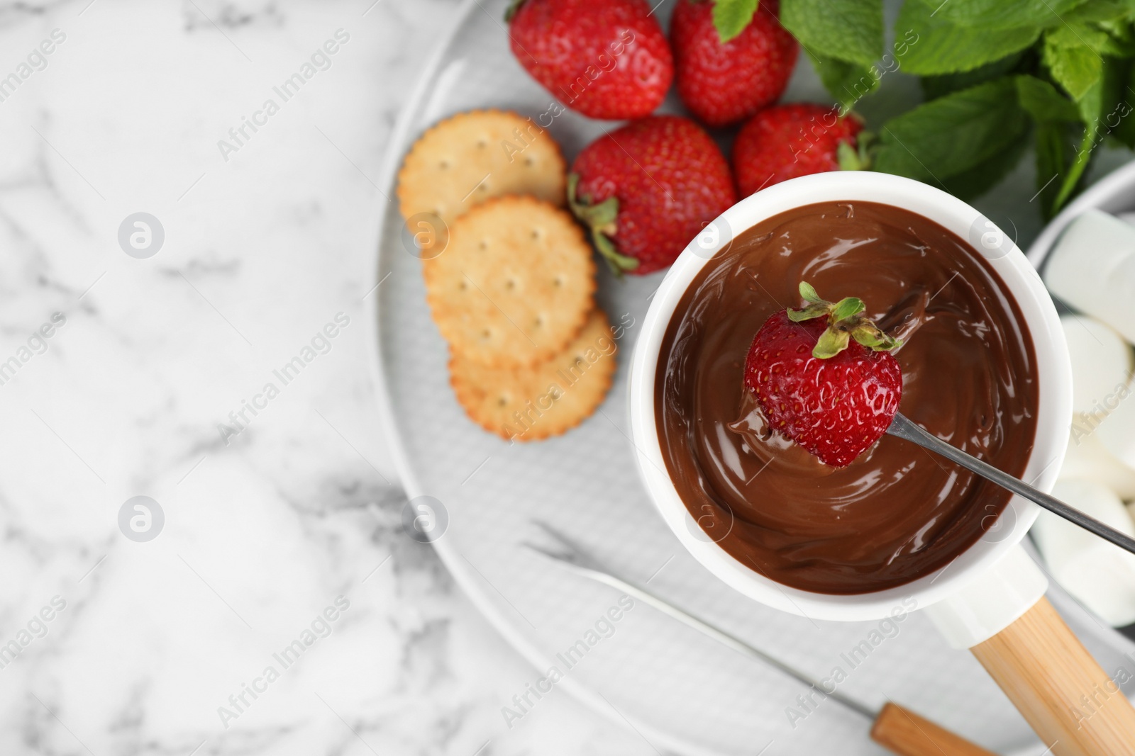 Photo of Fondue pot with chocolate and strawberry on white marble table, top view