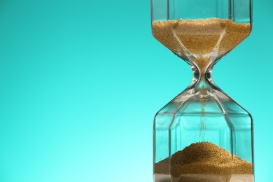 Hourglass with flowing sand on turquoise background, closeup. Space for text