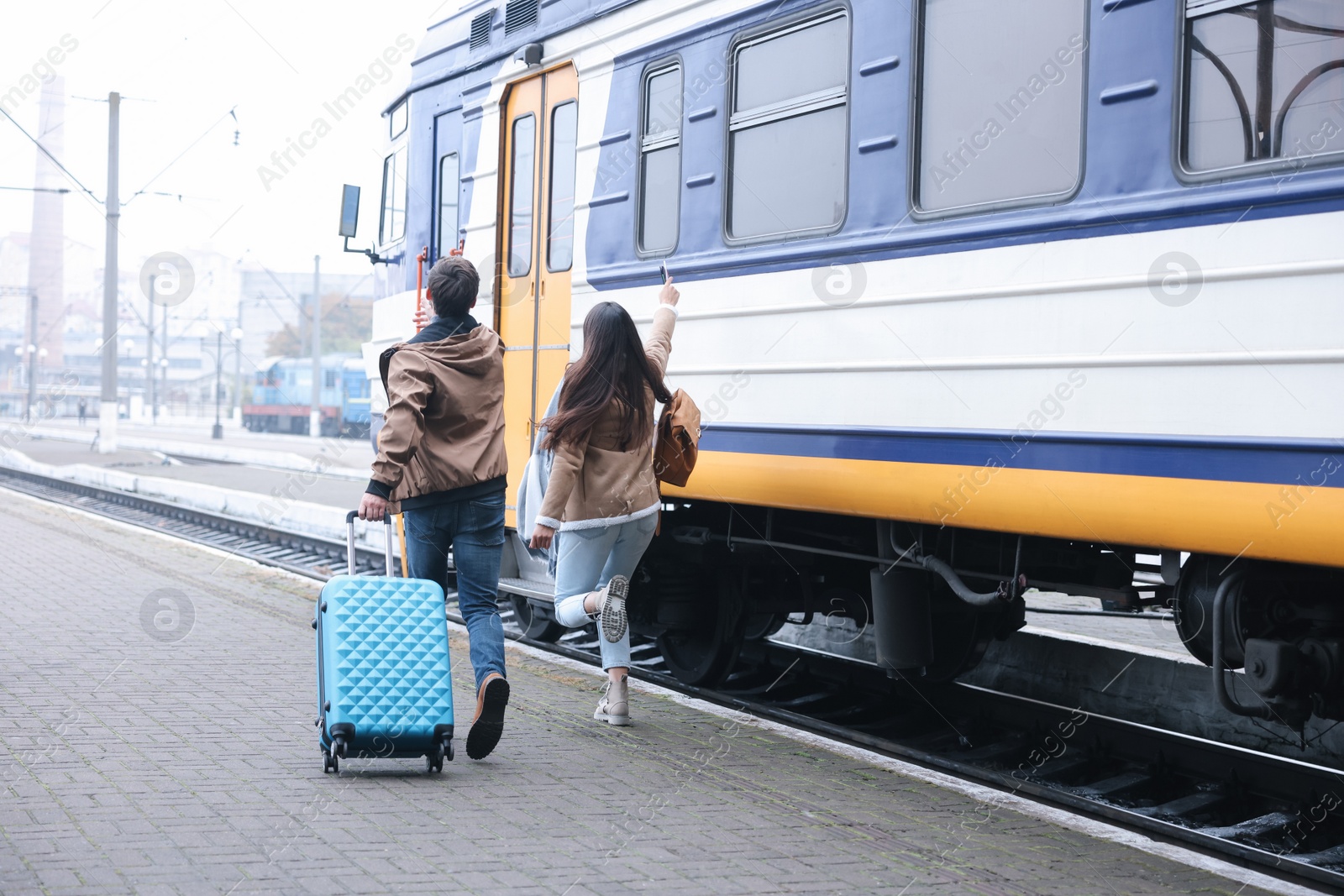 Photo of Being late. Couple with suitcase running towards train at station, back view. Space for text