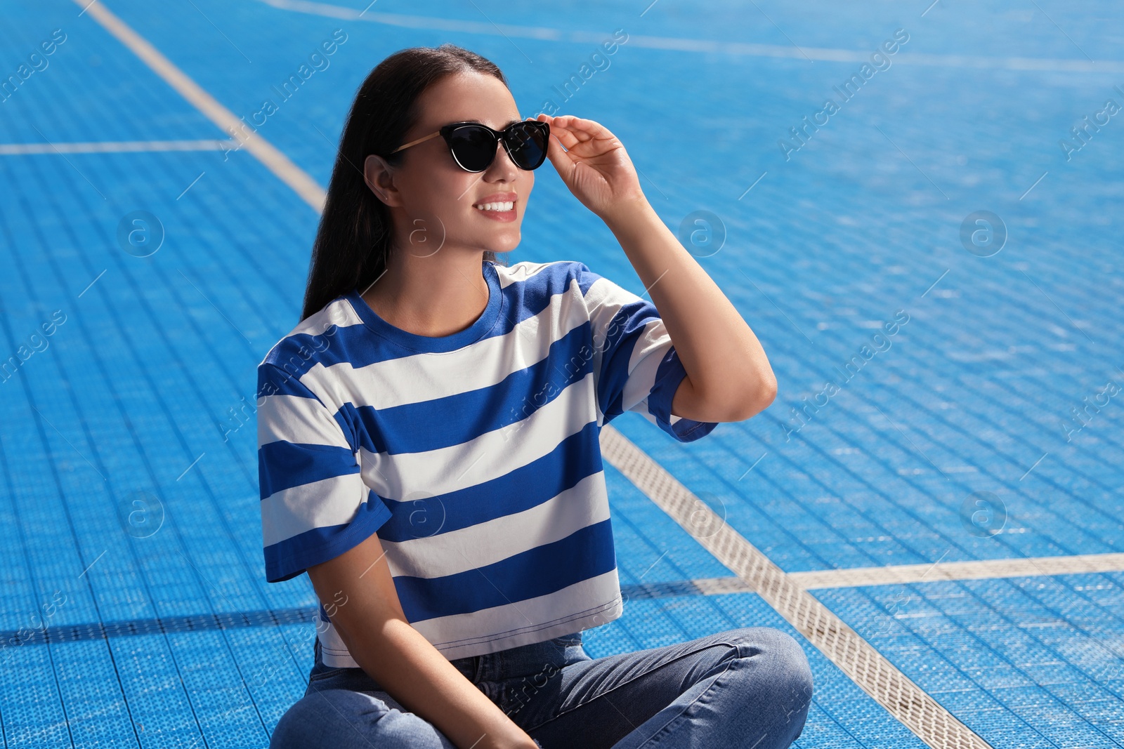 Photo of Beautiful smiling woman in sunglasses on blue floor covering outdoors, space for text