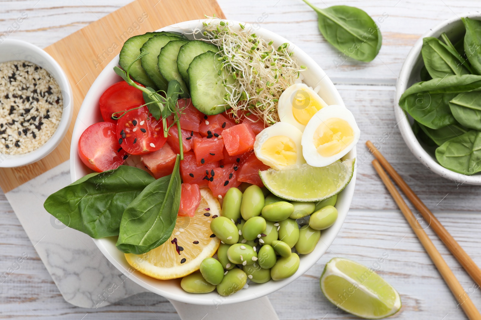 Photo of Delicious poke bowl with quail eggs, fish and edamame beans on white wooden table, flat lay