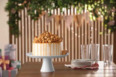 Photo of Caramel drip cake decorated with popcorn and pretzels near tableware on wooden table