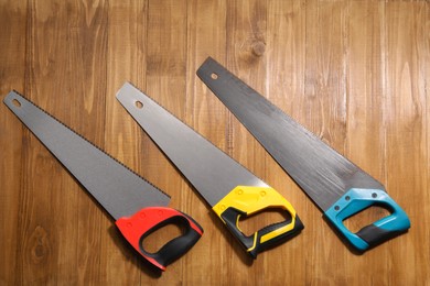 Saws with colorful handles on wooden background, flat lay