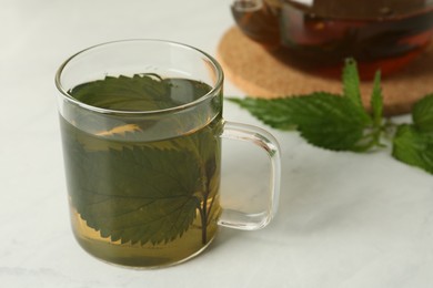 Photo of Glass cup of aromatic nettle tea on white table, space for text