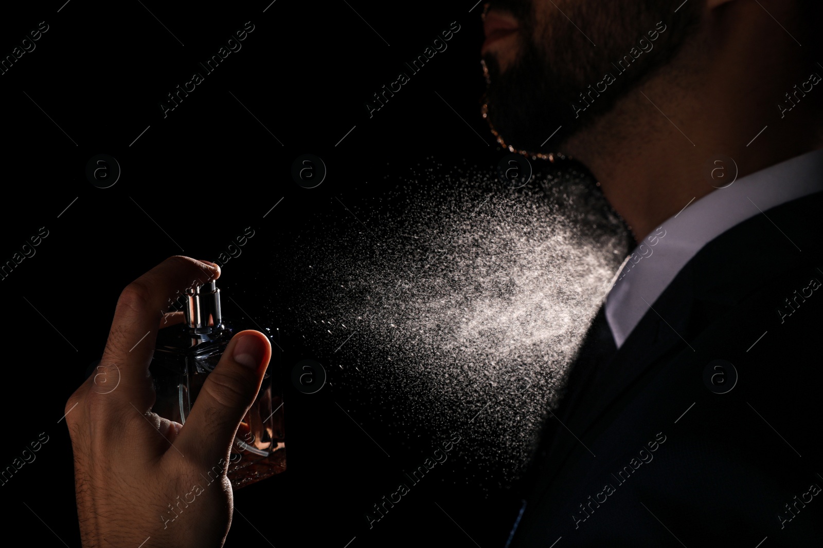 Photo of Man spraying luxury perfume on black background, closeup