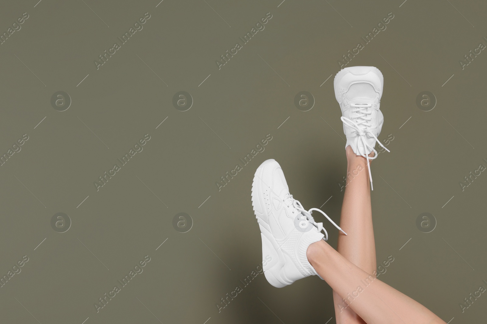 Photo of Woman wearing pair of new stylish sneakers on dark olive background, closeup. Space for text