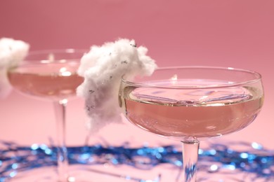 Photo of Tasty cocktails in glasses decorated with cotton candy and blue shiny streamers on pink background, closeup