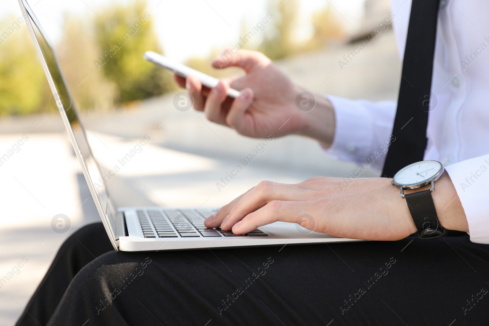 Image of Young man using phone and laptop outdoors, closeup