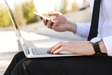 Young man using phone and laptop outdoors, closeup