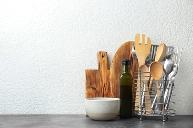 Photo of Set of kitchen utensils in stand on stone table near light wall. Space for text