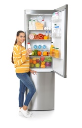 Photo of Young woman with bottle of yogurt near open refrigerator on white background