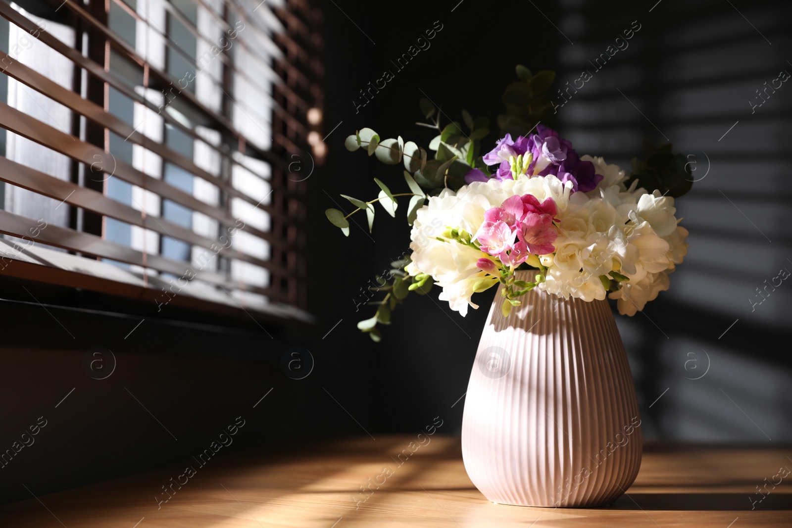 Photo of Beautiful bouquet with spring freesia flowers on sunlit wooden table in room, space for text